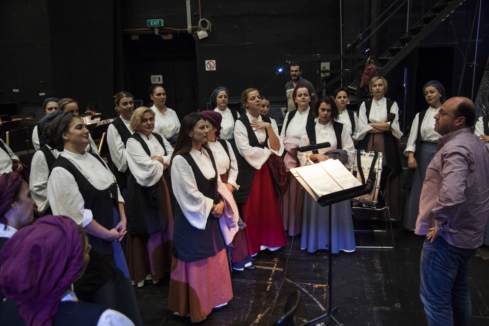 Η γυναικεία χορωδία τραγουδά πίσω από τη σκηνή υπό τη διεύθυνση του Αγαθάγγελου Γεωργακάτου 
