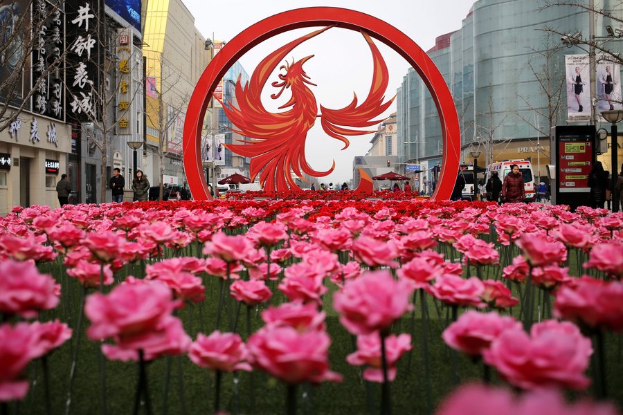 epa05720707 People walk by plastic flowers and a large rooster decoration set up for the upcoming Chinese Lunar New Year in Wangfujing Street in Beijing city, China, 16 January 2017. Chinese Lunar New Year, also called Spring Festival, which will fall on 28 January 2017, is the first day of the 'Year of the Rooster'.  EPA/WU HONG