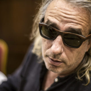 Μία μέρα, εντελώς ξαφνικά, επισκέφτηκαν τον Γιάννη Αγγελάκα δύο γοητευτικοί υπονομευτές κάθε ανθρώπινης βεβαιότητας με όρεξη για κουβέντα