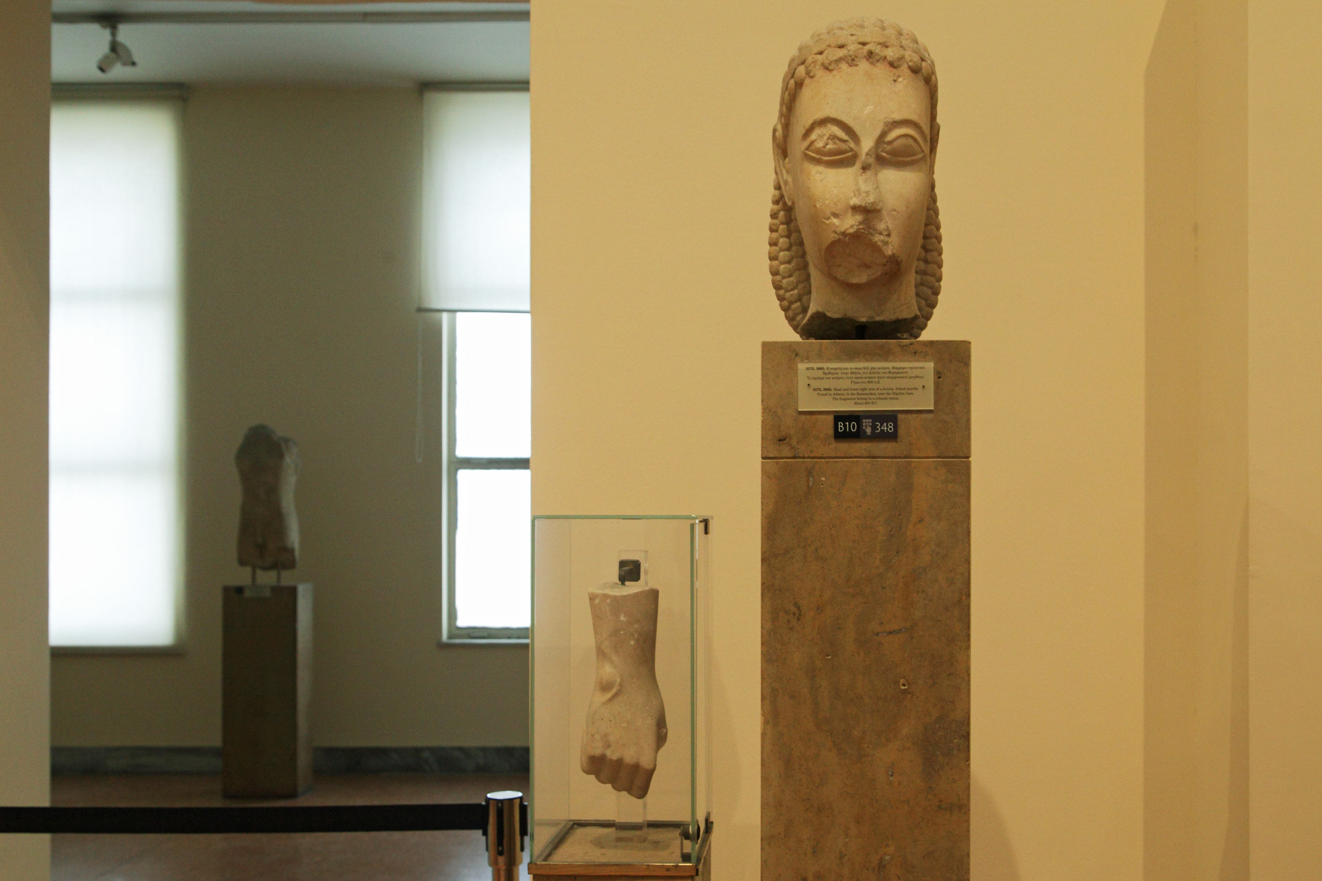 Μαρμάρινη κεφαλή κούρου, από ναξιακό μάρμαρο, βρέθηκε στον Κεραμεικό. Γύρω στο 600 π.Χ. Ο κούρος, στον οποίον ανήκε η κεφαλή όπως και το δεξί χέρι, ήταν υπερφυσικού μεγέθους (περίπου 3,00 μ.). Από τα αρχαιότερα έργα της μεγάλης πλαστικής. Αρχαιολογικό Μουσείο Αθηνών, Δεκέμβριος 2024.